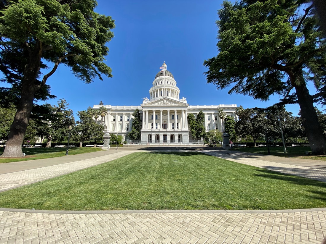 The California State Capitol in Sacramento, seen across the lawn with its dome above the trees.